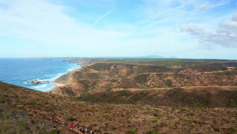 toma aérea en círculo que muestra a un grupo de excursionistas caminando en la parte superior de la costa del algarve durante un hermoso día soleado