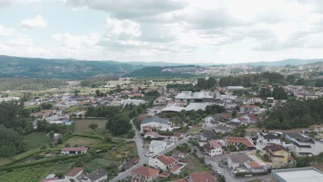 Aerial-view-of-a-small-town-with-surrounding-greenery-and-distant-mountains-under-a-cloudy-sky