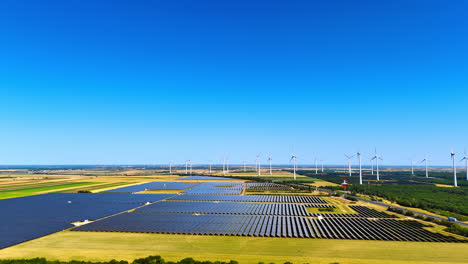 Renewable solar and wind energy. Solar panels cover the fields while wind turbines rotate in the background under a clear blue sky
