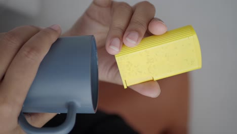 person holding a yellow container and a gray mug