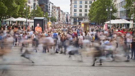 a bustling urban scene captured in motion: busy pedestrians fill the plaza, interacting amidst the energy of city life, showcasing movement and vibrancy.