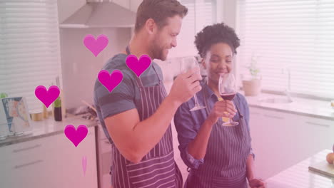 Animation-of-hearts-over-diverse-couple-cooking-together-and-drinking-wine-in-kitchen-at-home