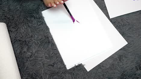 Woman-uses-toes-to-hold-paint-brush-with-pink-purple-paint-to-write-hi-on-white-paper