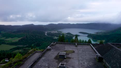 Drone-flying-above-the-abandoned-hotel,-Monte-palace,-towards-the-green-mountains-and-lakes