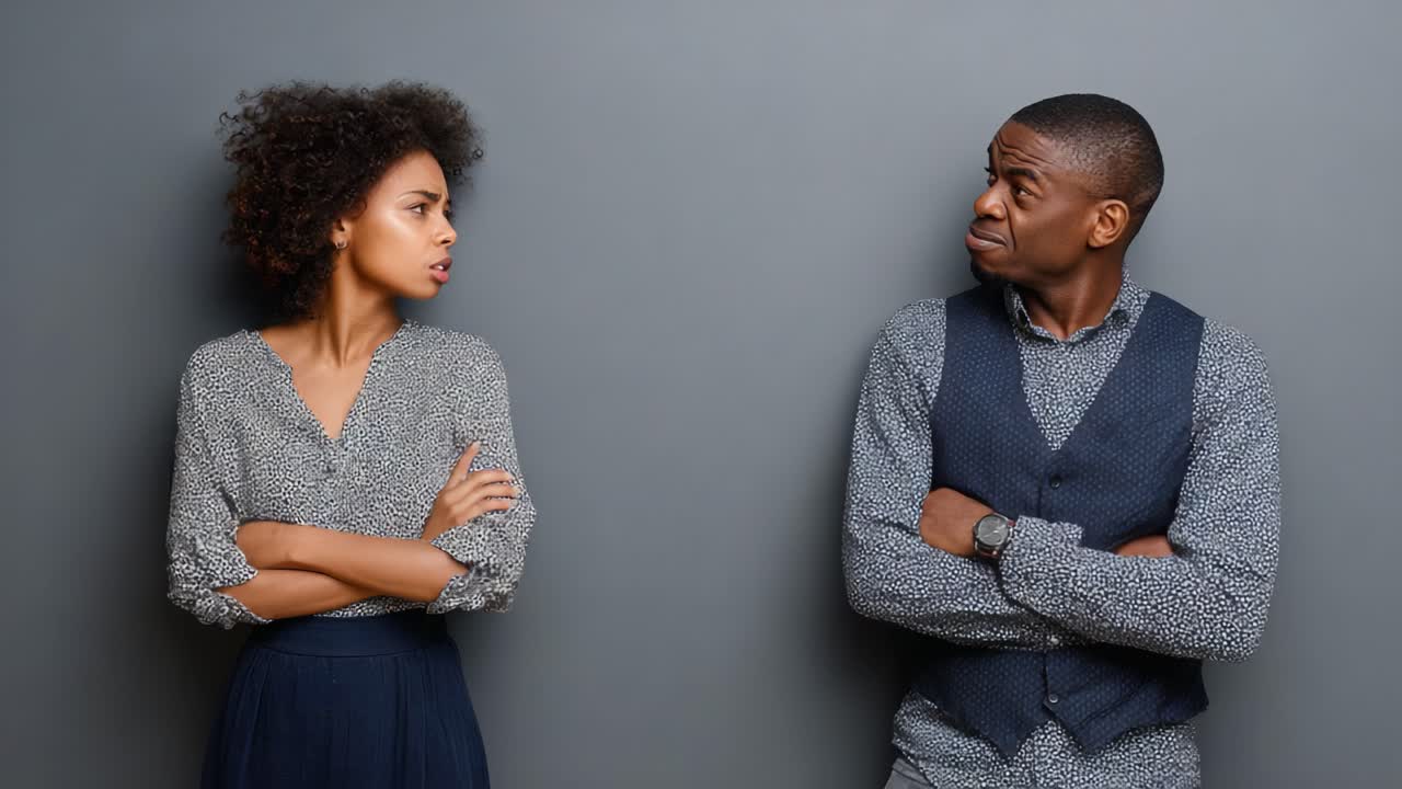 A tense moment captured between two individuals standing against a neutral gray backdrop, displaying emotions of disagreement and contemplation in their expressions and body language