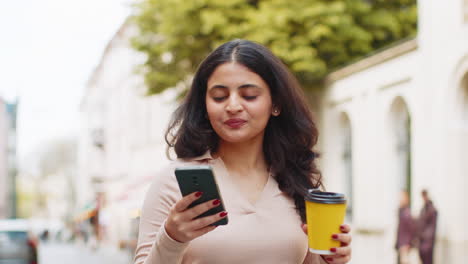 Woman-use-smartphone-texting-social-media-messages-enjoying-morning-coffee-hot-drink-on-city-street