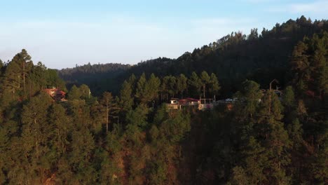 aerial view of hilltop buildings and houses in oaxaca state highlands, touristic lookout on mountain range on golden hour sunlight, revealing drone shot