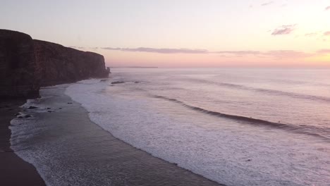 drone shot with the coast with cliffs at sunset and surfers