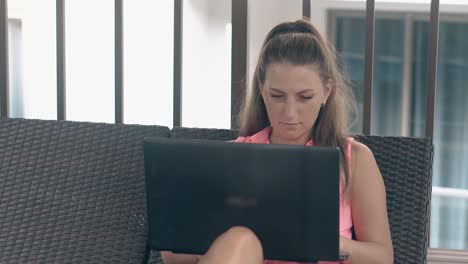 tanned woman in earings sits on lounger types on laptop