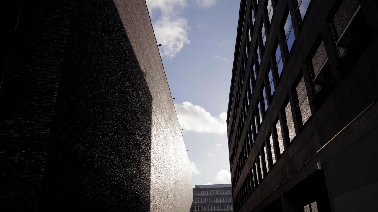 interacción dramática de luz y sombra entre edificios modernos de colonia. una toma urbana minimalista con texturas y reflejos bajo un cielo despejado.
