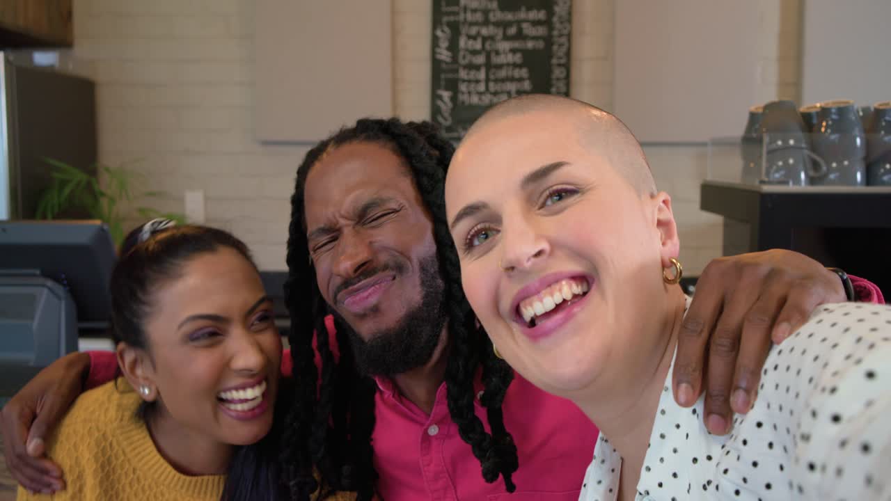 Três amigos avistando a câmera no balcão do café, de braços dados, sorrindo, rindo enquanto tiram uma selfie