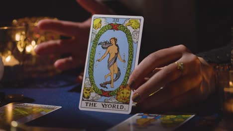 primer plano de una mujer dando una lectura de cartas del tarot en una mesa a la luz de las velas sosteniendo la carta del mundo 4