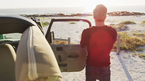 caucasian man in sunglasses getting out of car and closing door on sunny day at the beach