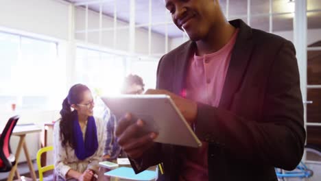 Male-business-executive-using-digital-tablet-while-coworker-interacting-in-background