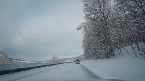 POV-video-of-a-daytime-drive-through-the-snowy-roads-of-Norway's-Western-Fjords,-surrounded-by-tall,-snow-covered-mountains-with-trees