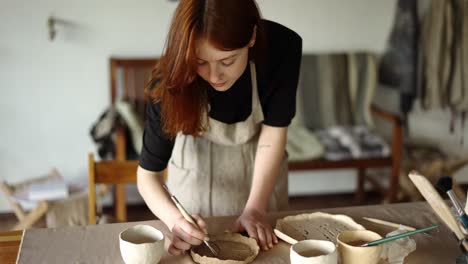 A-red-haired-potter-girl-draws-on-clay-using-special-tools