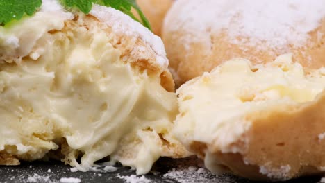 baked custard eclairs and sprinkled with powdered sugar and decorated with a mint leaf on a black board