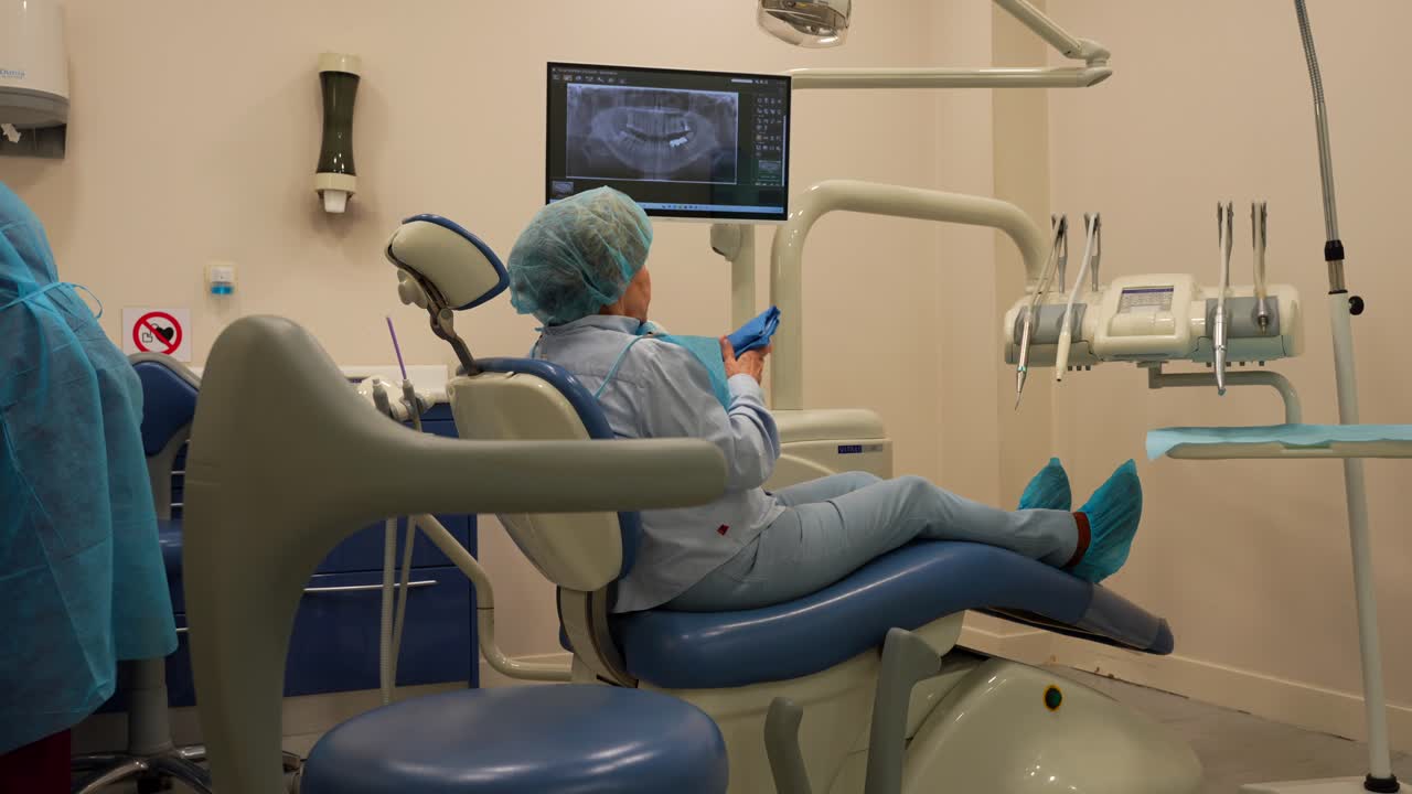 anciana acostada en una silla dental sosteniendo una servilleta para el alivio del dolor de dientes, rayos x visibles