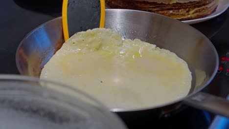 un primer plano de la masa de panqueque cocinando en una sartén en una estufa con panqueques apilados en el fondo