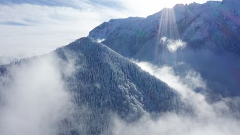 Sun-rays-over-snow-covered-Bucegi-Mountains,-aerial-view,-misty-forest