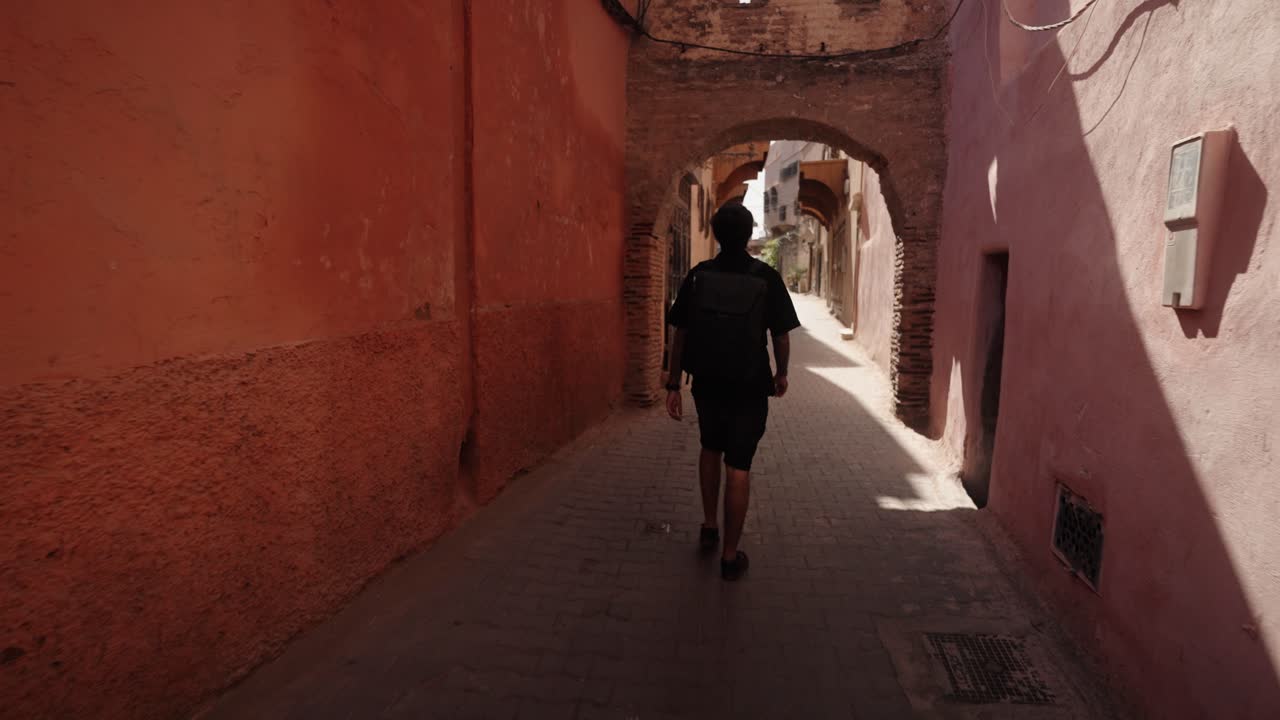 Traveler walks under a stone arch in a narrow street inside Marrakech Medina