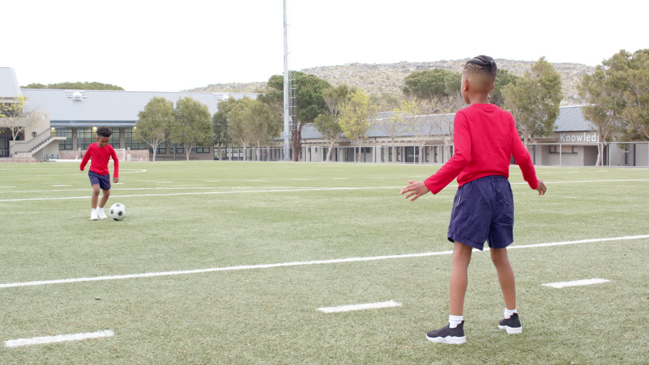 Multiracial boys playing soccer on school field, wearing red shirts, enjoying outdoor activity