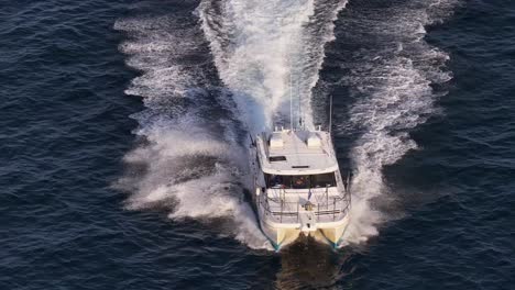 a commercial fishing charter boat cruises rapidly over rough ocean waters at sunset, captured in a dynamic aerial drone flyover with dramatic lighting