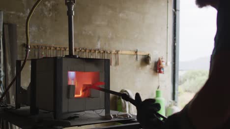 Caucasian-male-blacksmith-holding-hot-metal-tool-in-kiln-with-tongs-in-workshop