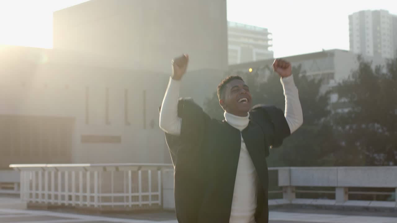 Pullback urging African American male graduate on rooftop tossing cap upward celebrating graduation