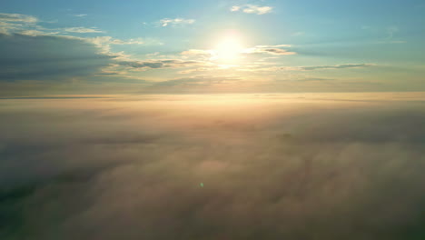 Sunshine glowing high in the sky above countryside covered in thick fog, aerial view