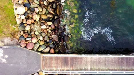 top down angle of waves softly lapping against a rocky pier