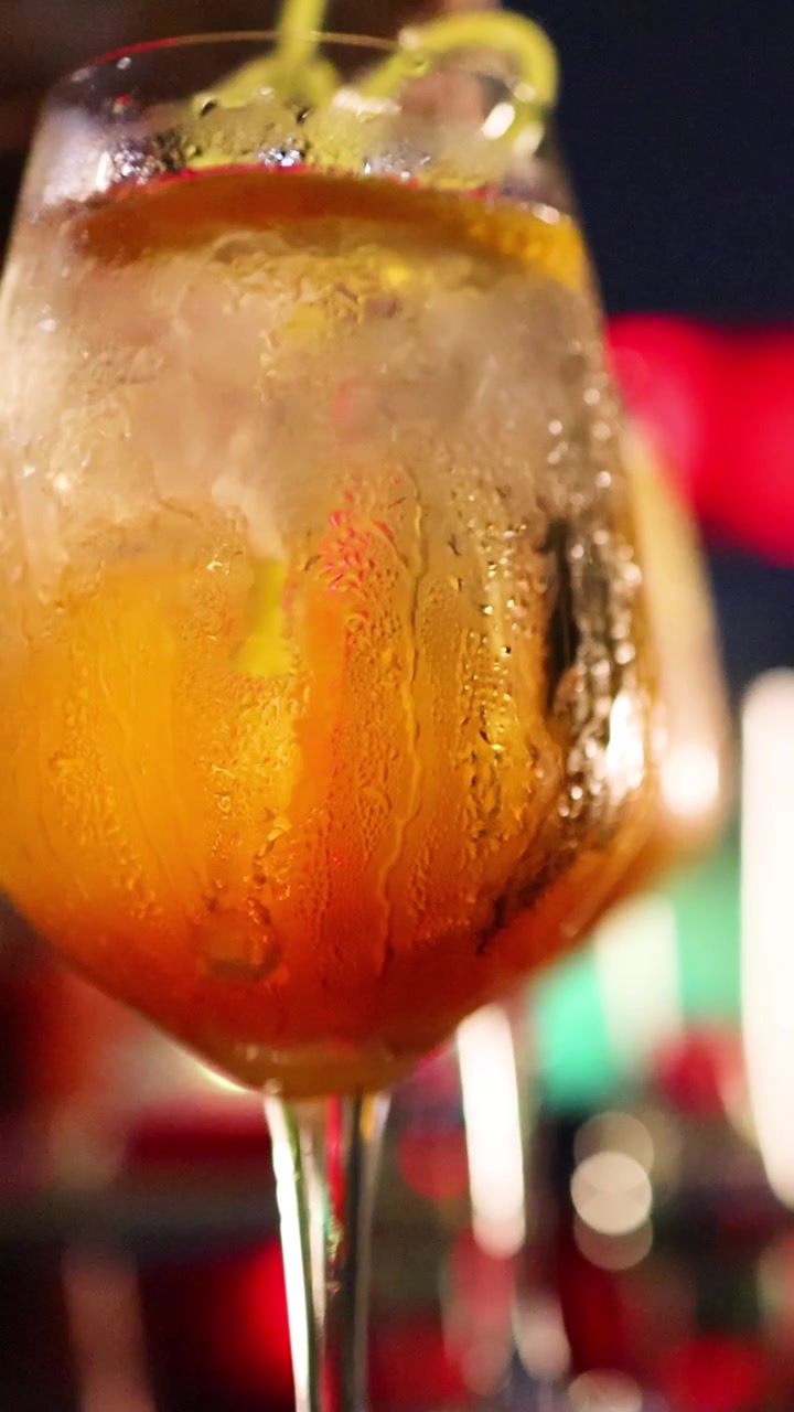 Un primo piano di un cocktail ghiacciato in un bicchiere con stelo, guarnito con una scorza di limone, con luci bokeh colorate in un vivace ambiente da bar notturno