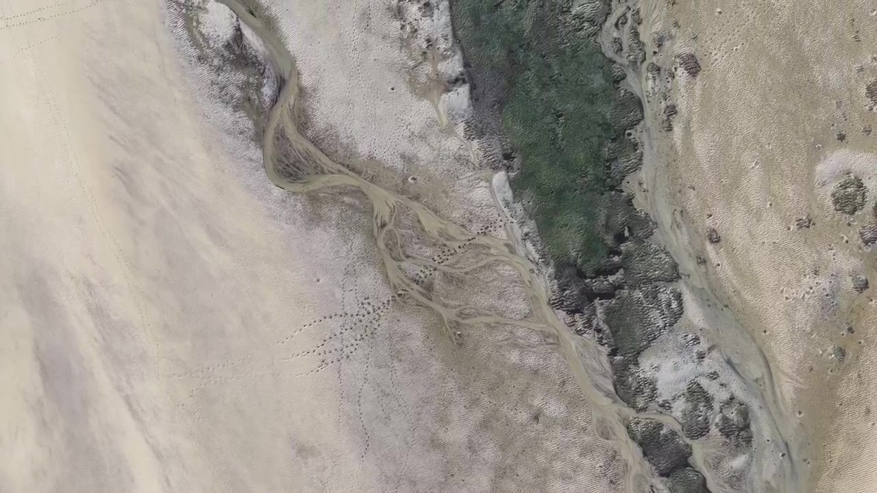 Riprese con drone zenitali che rivelano motivi naturali astratti formati da texture di sabbia, acqua e terra.