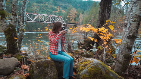 photographer woman takes polaroid photo along riverside among fall colors