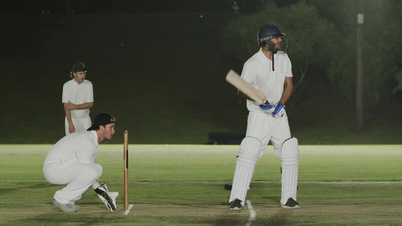 Battitore di cricket che si sposta verso la linea di battuta mentre il lanciatore lancia, difendendo i wicket mentre sfere blu ruotano