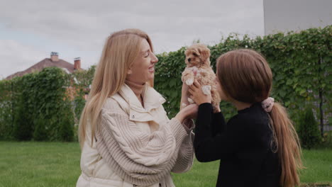 Mom-and-daughter-play-with-a-small-puppy-in-the-backyard-of-the-house