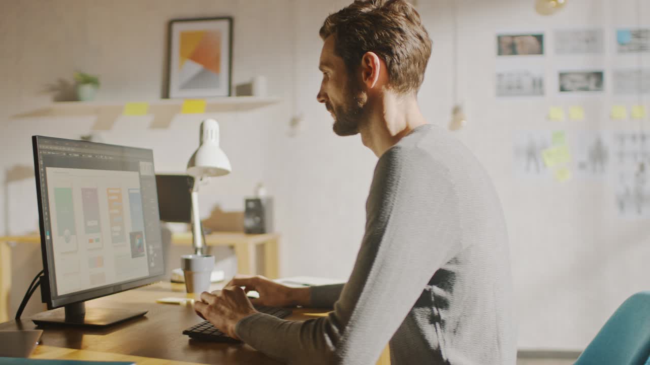 Creative Designer Sitting at His Desk in Office Studio Working on a Desktop Computer with Smartphone Software Development Application on Screen. Web, App Developer. 360 Degree Tracking Arc Shot