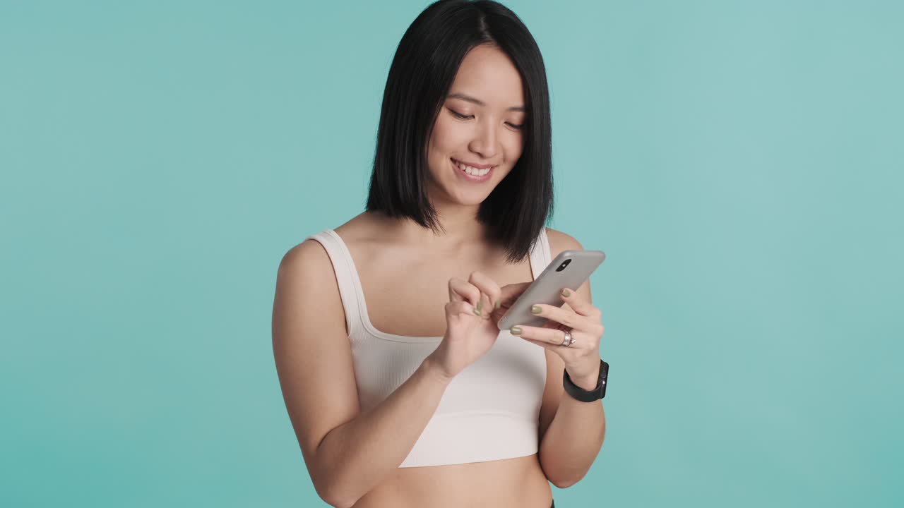 아시아 여성이 스마트폰으로 문자 메시지를 보내며 미소 짓고 있습니다.