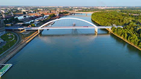 flight over the blue waterscape of the danube. footage at the beautiful appolo bridge with a riverboat passing under. bratislava, slovakia