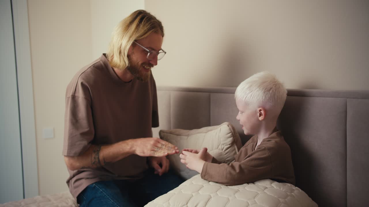 수염과 안경을 가진 행복한 아버지 남자가 주말 휴가 동안 회색 노트북 근처의 크림 침대에서 재미있게 놀고 있습니다.