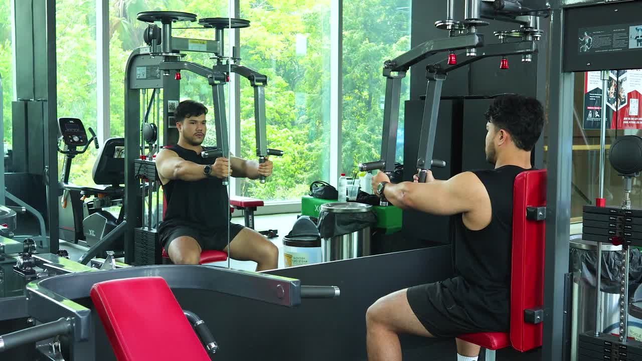Young athletic man using chest fly machine in bright, modern gym with large windows