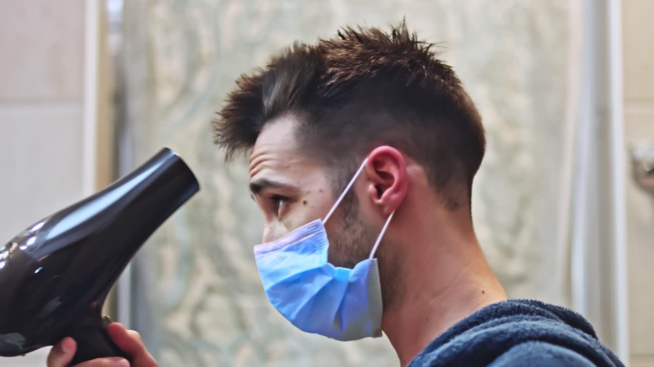 un hombre guapo se seca el pelo en el baño con una máscara médica protectora
