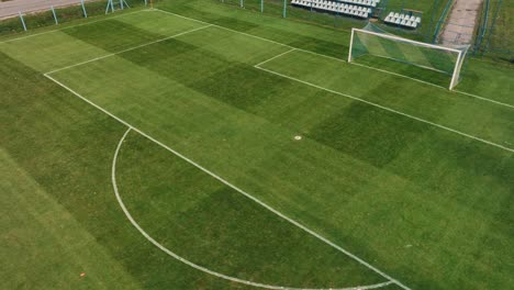 High-angle-drone-shot-of-a-soccer-football-net-with-a-small-tribune-on-the-background-during-sunny-autumn-day