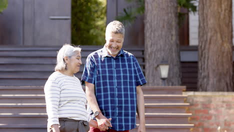 Feliz-Pareja-De-Ancianos-Birraciales-Hablando-Y-Tomados-De-La-Mano-En-Un-Jardín-Soleado