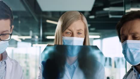 close-up view of caucasian male and female doctors in medical masks speaking and discussing xray scan and typing on tablet device in hospital office