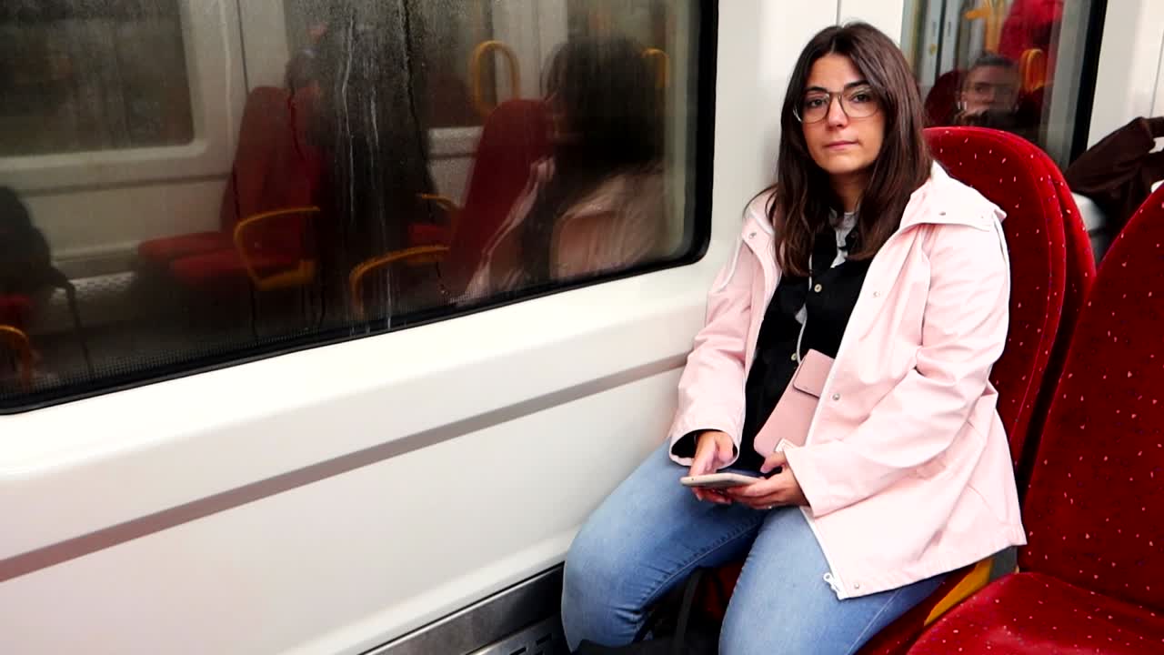 mujer en tren con abrigo de lluvia rosa y un teléfono