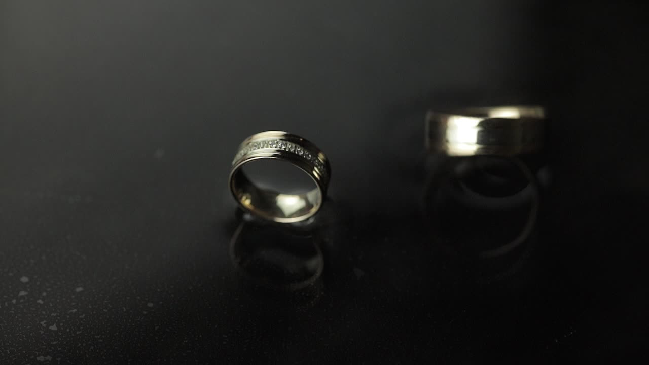 Wedding rings on dark water surface shining with light. One of rings rotates