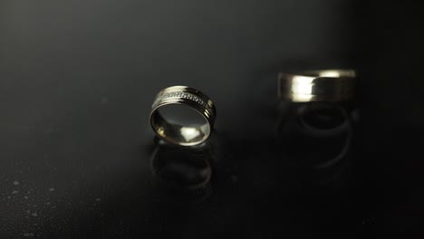 Anillos-De-Boda-En-La-Superficie-Del-Agua-Oscura-Brillando-Con-Luz.-Uno-De-Los-Anillos-Gira