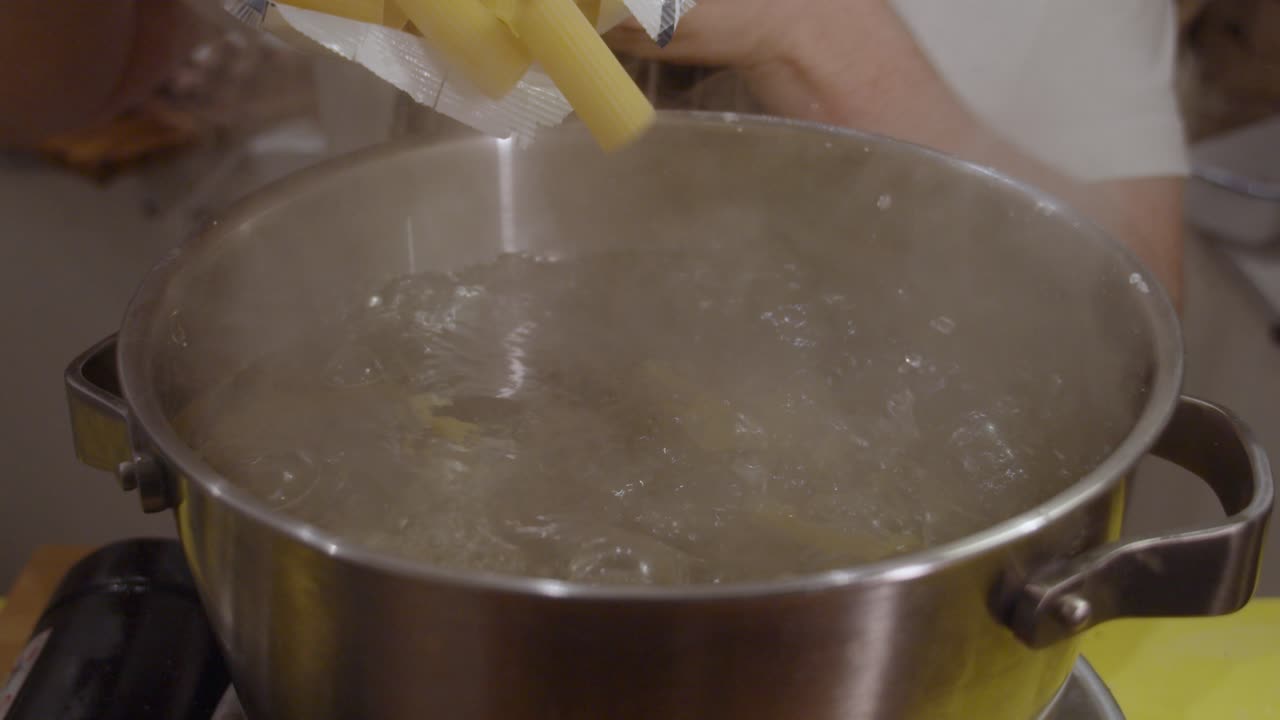 Echando pasta del paquete a la olla con agua hirviendo