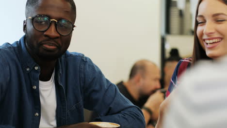 close-up view of multiethnic group of friends talking and laughing sitting at a table in a cafe